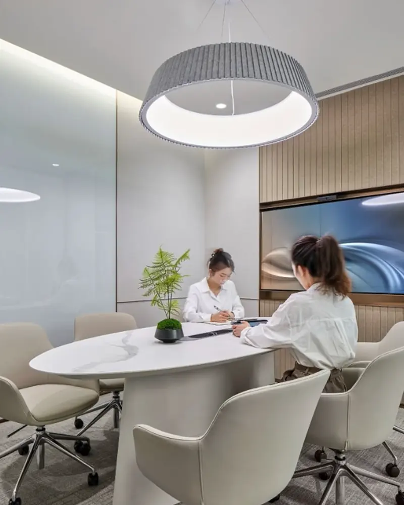 Small meeting room with an oval stone table, upholstered chairs and a wall-mounted display