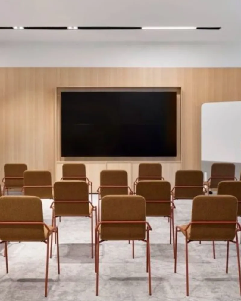 Training and townhall room with theatre-style upholstered chairs, an oak feature wall and a large display